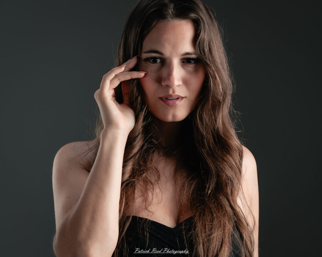A studio portrait a poised female model in a sleek black dress, photographed under controlled lighting on August 23, 2025.