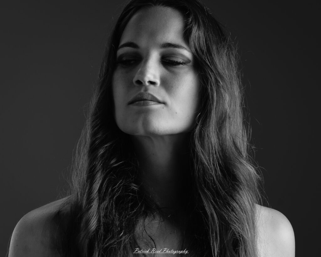 A studio portrait a poised female model in a sleek black dress, photographed under controlled lighting on August 23, 2025.