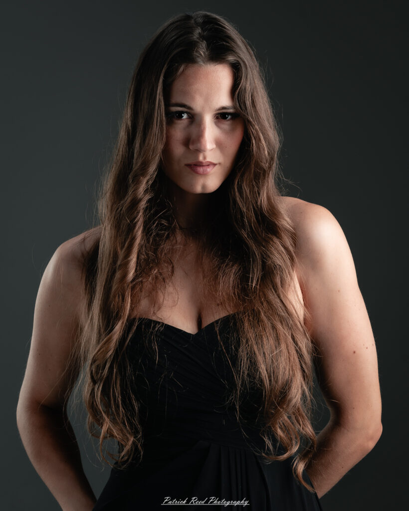 A studio portrait a poised female model in a sleek black dress, photographed under controlled lighting on August 23, 2025.