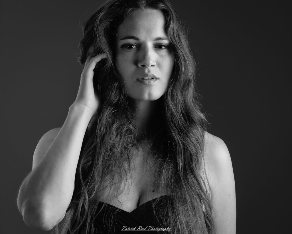 A studio portrait a poised female model in a sleek black dress, photographed under controlled lighting on August 23, 2025.