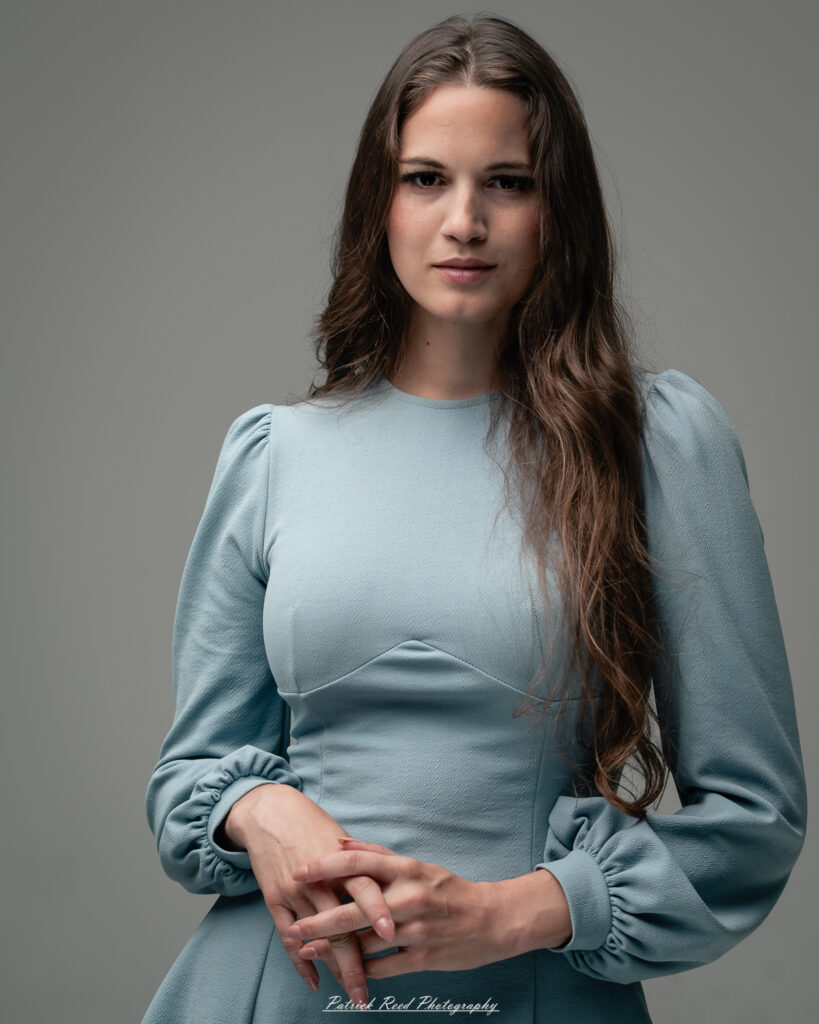 A studio portrait a confident female model in an elegant blue dress, photographed with dramatic studio lighting on August 23, 2025.