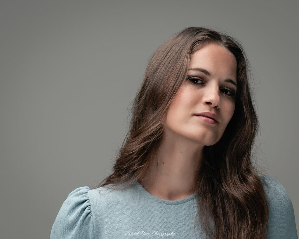 A studio portrait a confident female model in an elegant blue dress, photographed with dramatic studio lighting on August 23, 2025.