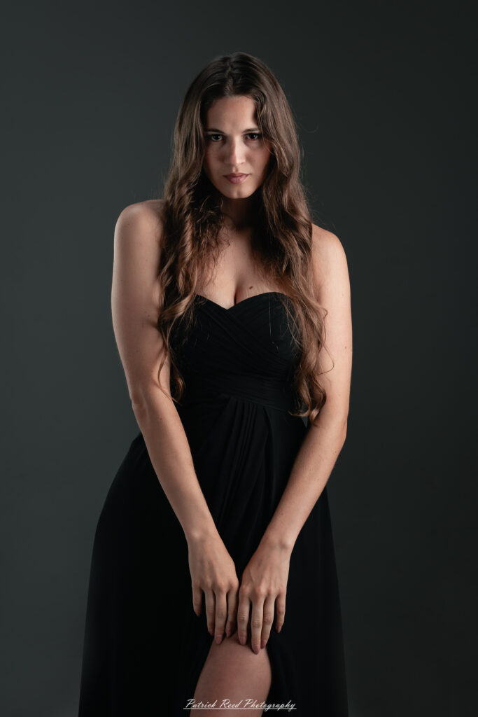 A studio portrait a poised female model in a sleek black dress, photographed under controlled lighting on August 23, 2025.
