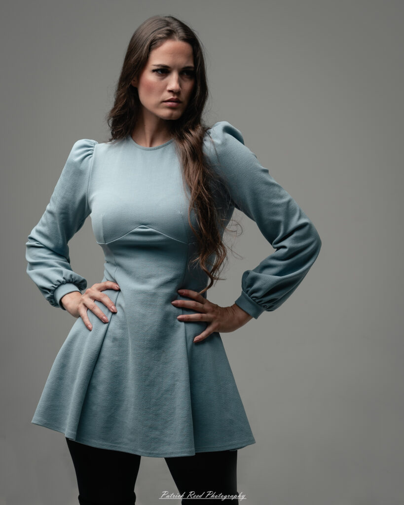 A studio portrait a confident female model in an elegant blue dress, photographed with dramatic studio lighting on August 23, 2025.
