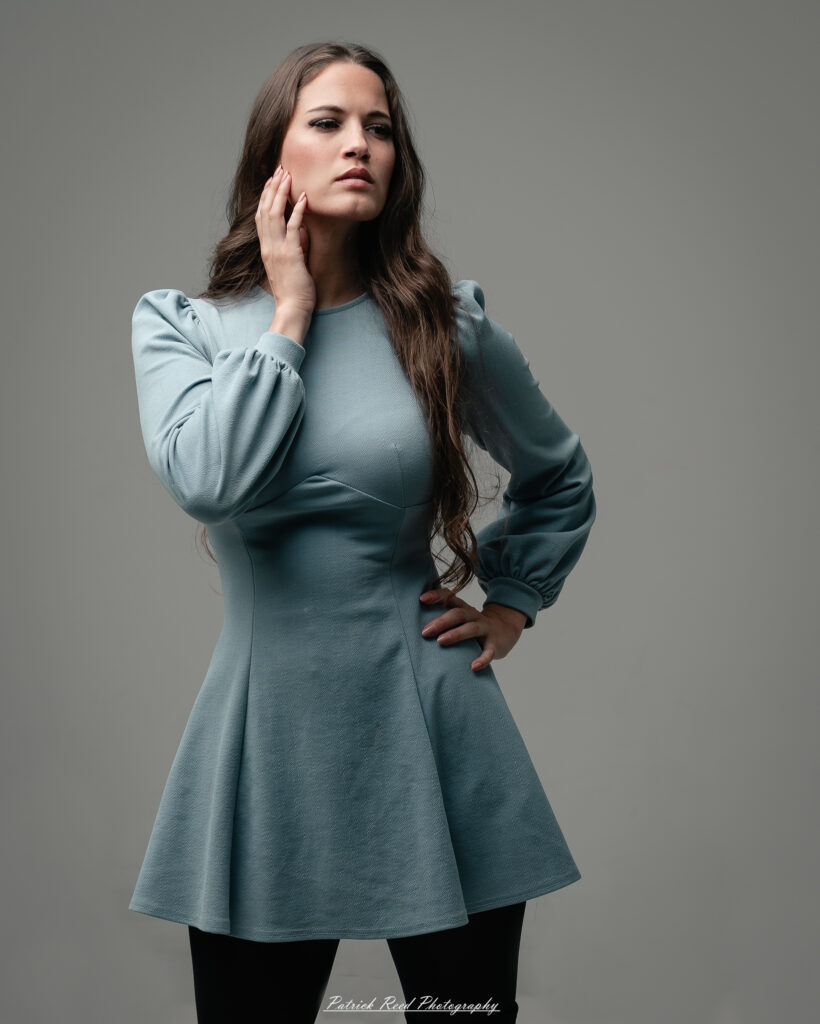 A studio portrait a confident female model in an elegant blue dress, photographed with dramatic studio lighting on August 23, 2025.
