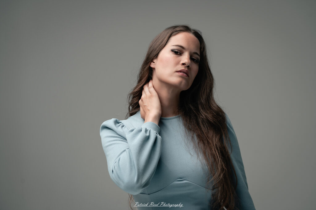 A studio portrait a confident female model in an elegant blue dress, photographed with dramatic studio lighting on August 23, 2025.