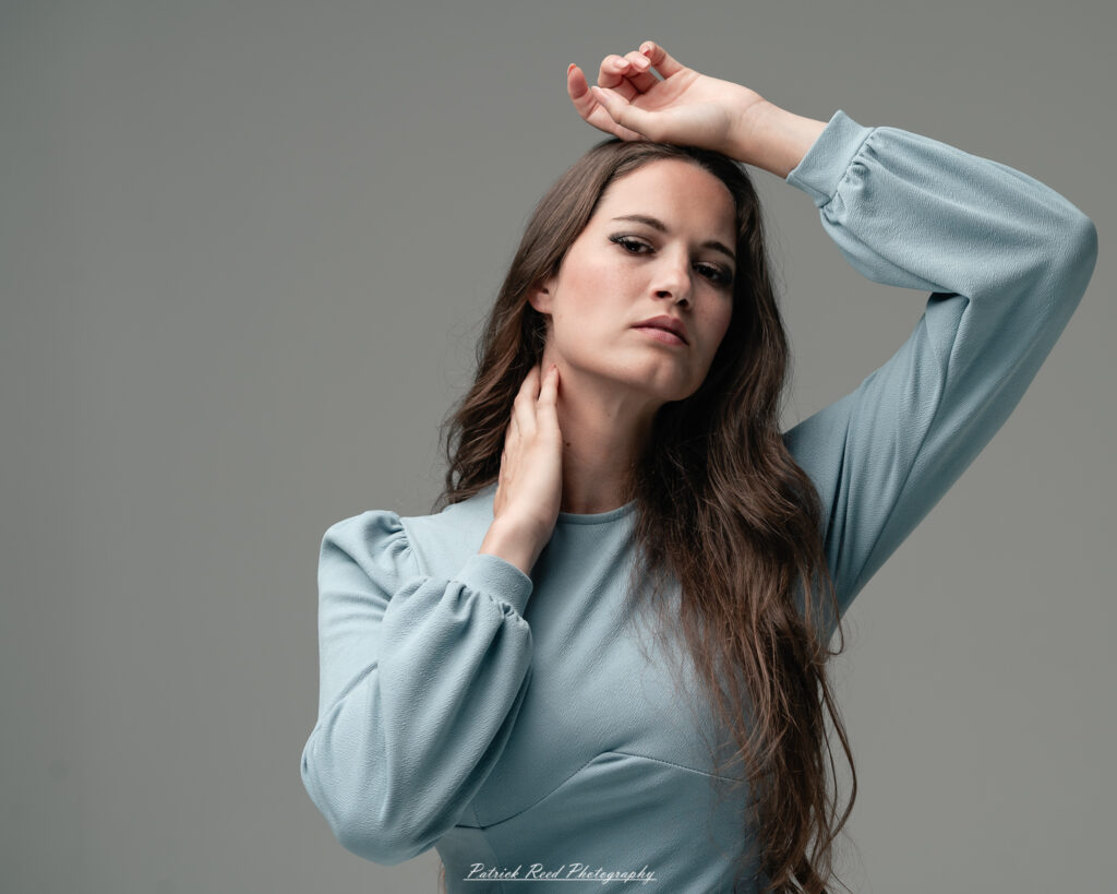A studio portrait a confident female model in an elegant blue dress, photographed with dramatic studio lighting on August 23, 2025.