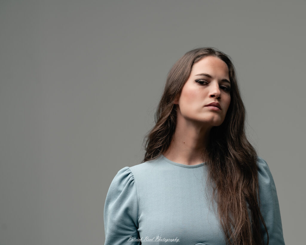 A studio portrait a confident female model in an elegant blue dress, photographed with dramatic studio lighting on August 23, 2025.
