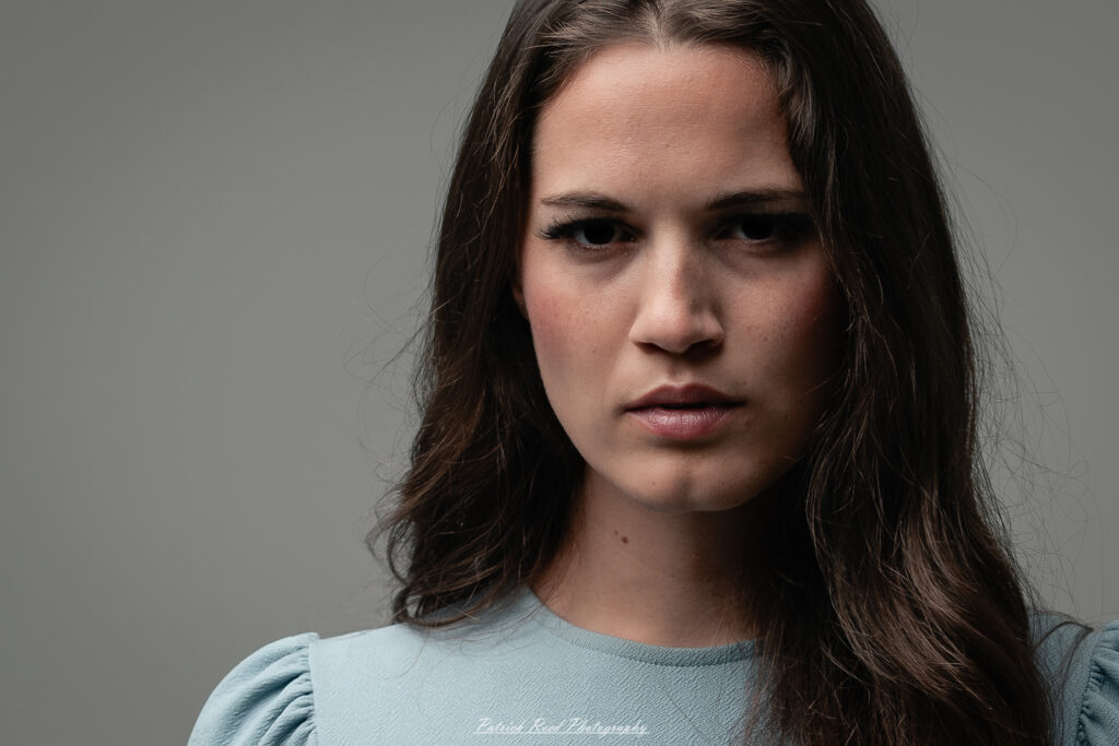A studio portrait a confident female model in an elegant blue dress, photographed with dramatic studio lighting on August 23, 2025.
