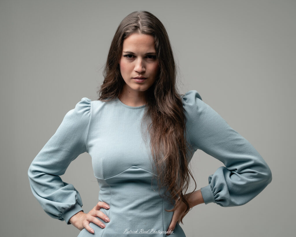 A studio portrait a confident female model in an elegant blue dress, photographed with dramatic studio lighting on August 23, 2025.