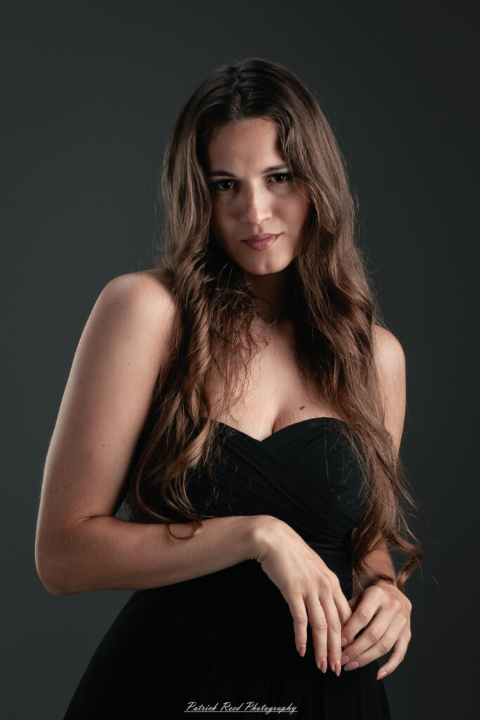 A studio portrait a poised female model in a sleek black dress, photographed under controlled lighting on August 23, 2025.