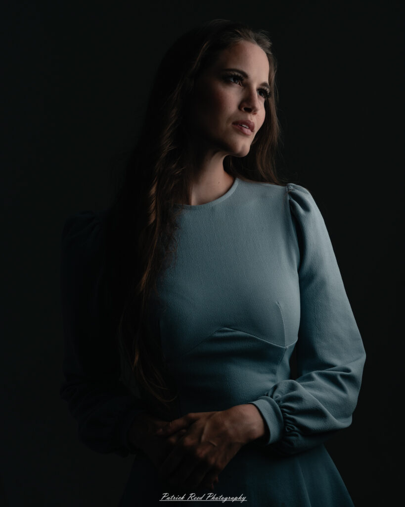 A studio portrait a confident female model in an elegant blue dress, photographed with dramatic studio lighting on August 23, 2025.