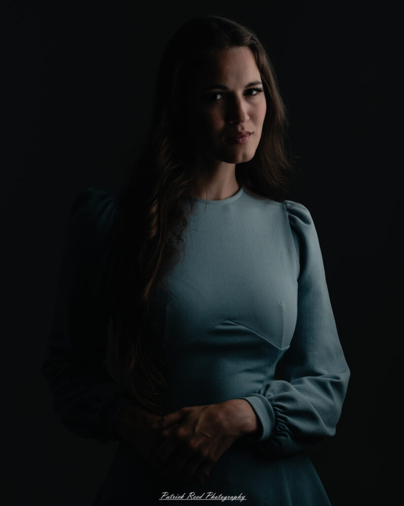 A studio portrait a confident female model in an elegant blue dress, photographed with dramatic studio lighting on August 23, 2025.