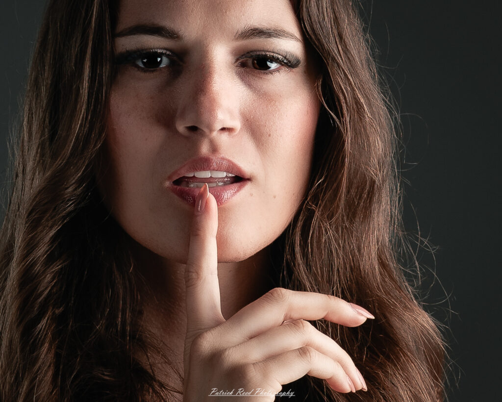A studio portrait a poised female model in a sleek black dress, photographed under controlled lighting on August 23, 2025.
