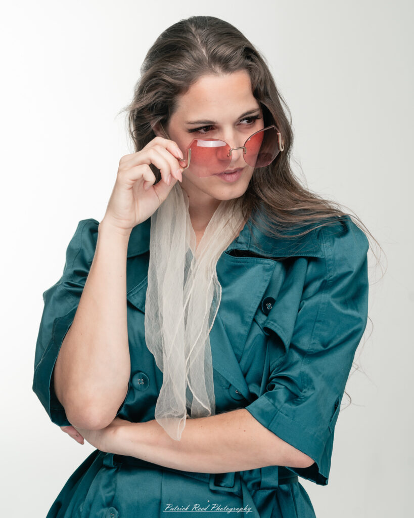 A dramatic studio portrait of woman wearing a stylish teal trench coat, photographed on August 23, 2025, with moody, directional lighting for a bold and modern look.