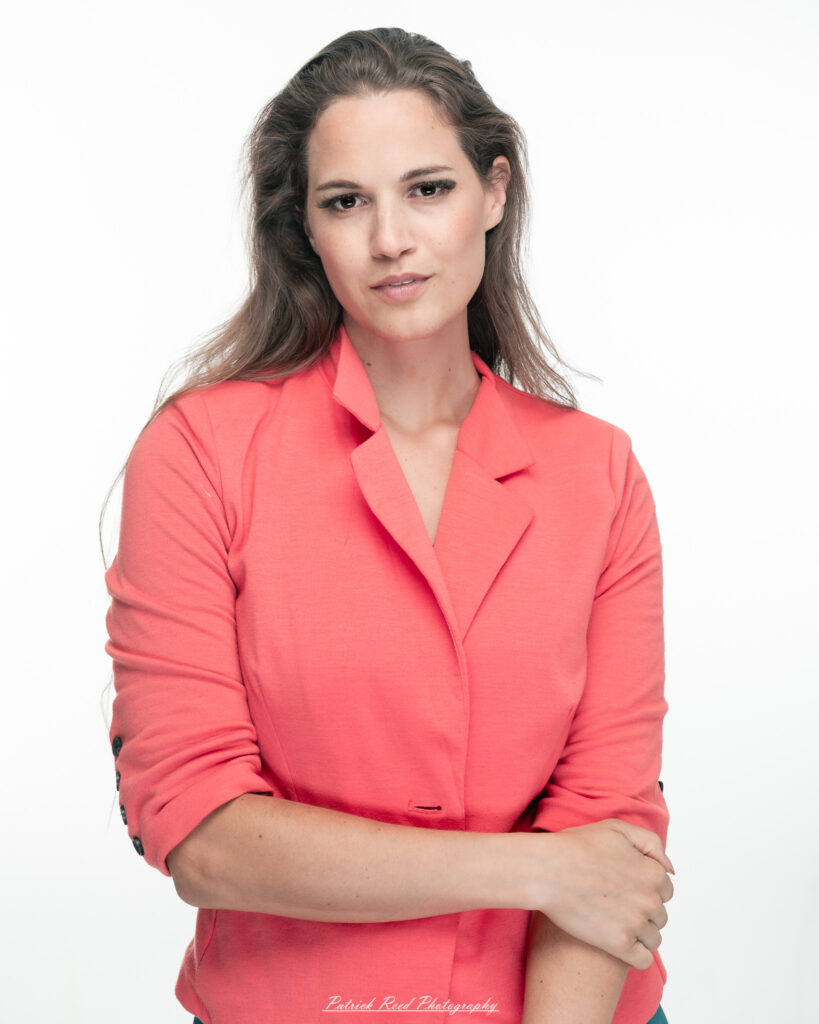 A dramatic studio portrait of a woman in a pink shirt, photographed on August 23, 2025, with bold lighting that emphasizes contrast and texture.
