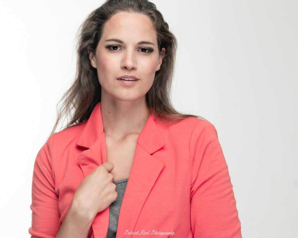 A dramatic studio portrait of a woman in a pink shirt, photographed on August 23, 2025, with bold lighting that emphasizes contrast and texture.