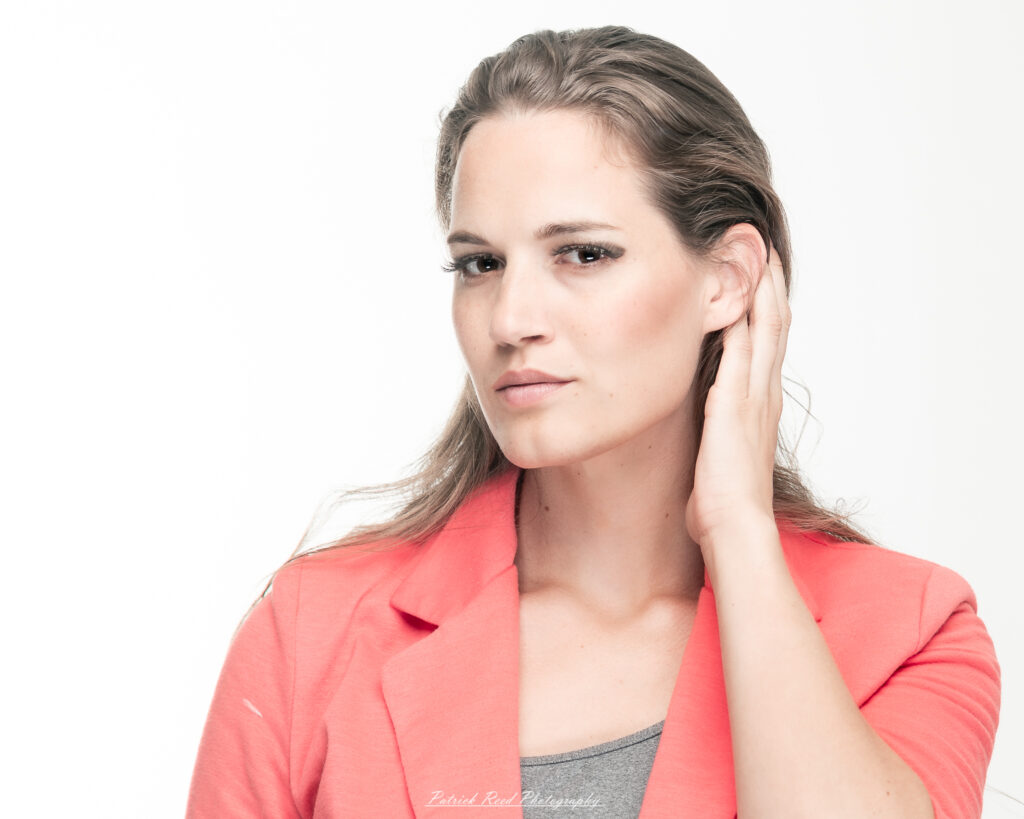 A dramatic studio portrait of a woman in a pink shirt, photographed on August 23, 2025, with bold lighting that emphasizes contrast and texture.