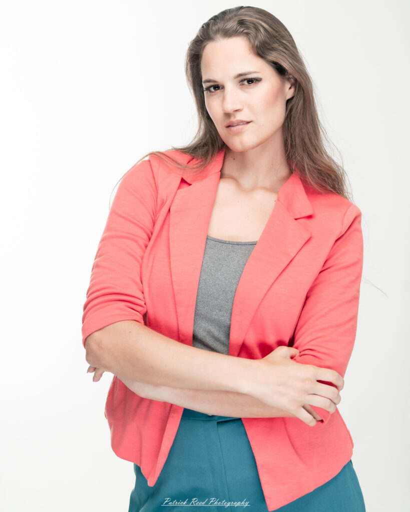 A dramatic studio portrait of a woman in a pink shirt, photographed on August 23, 2025, with bold lighting that emphasizes contrast and texture.