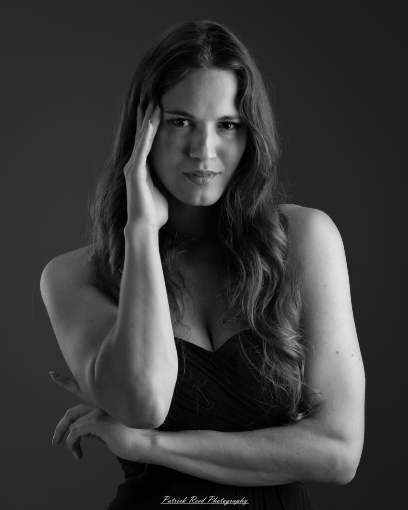 A studio portrait a poised female model in a sleek black dress, photographed under controlled lighting on August 23, 2025.