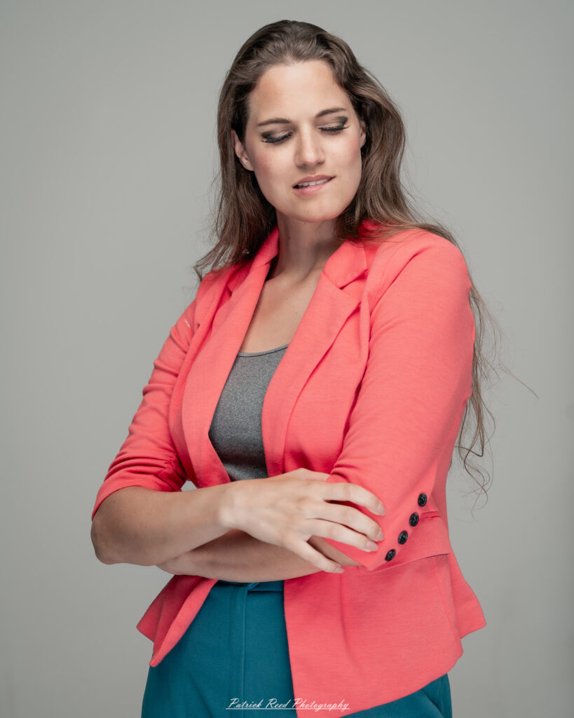 A dramatic studio portrait of a woman in a pink shirt, photographed on August 23, 2025, with bold lighting that emphasizes contrast and texture.