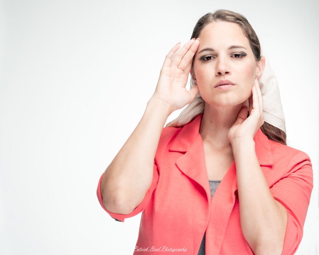 A dramatic studio portrait of a woman in a pink shirt, photographed on August 23, 2025, with bold lighting that emphasizes contrast and texture.