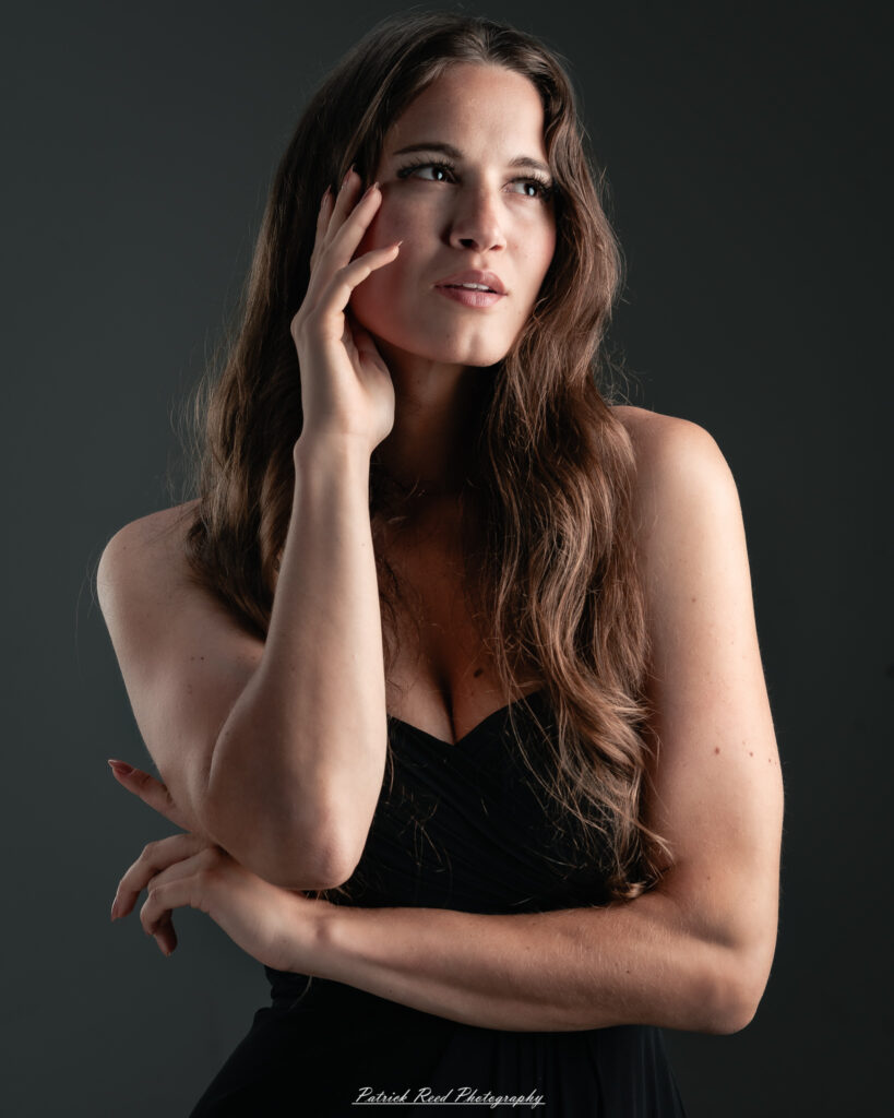 A studio portrait a poised female model in a sleek black dress, photographed under controlled lighting on August 23, 2025.