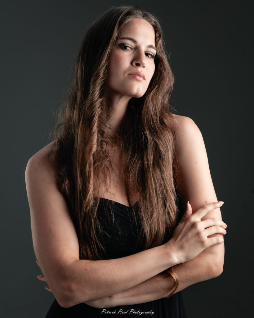 A studio portrait a poised female model in a sleek black dress, photographed under controlled lighting on August 23, 2025.