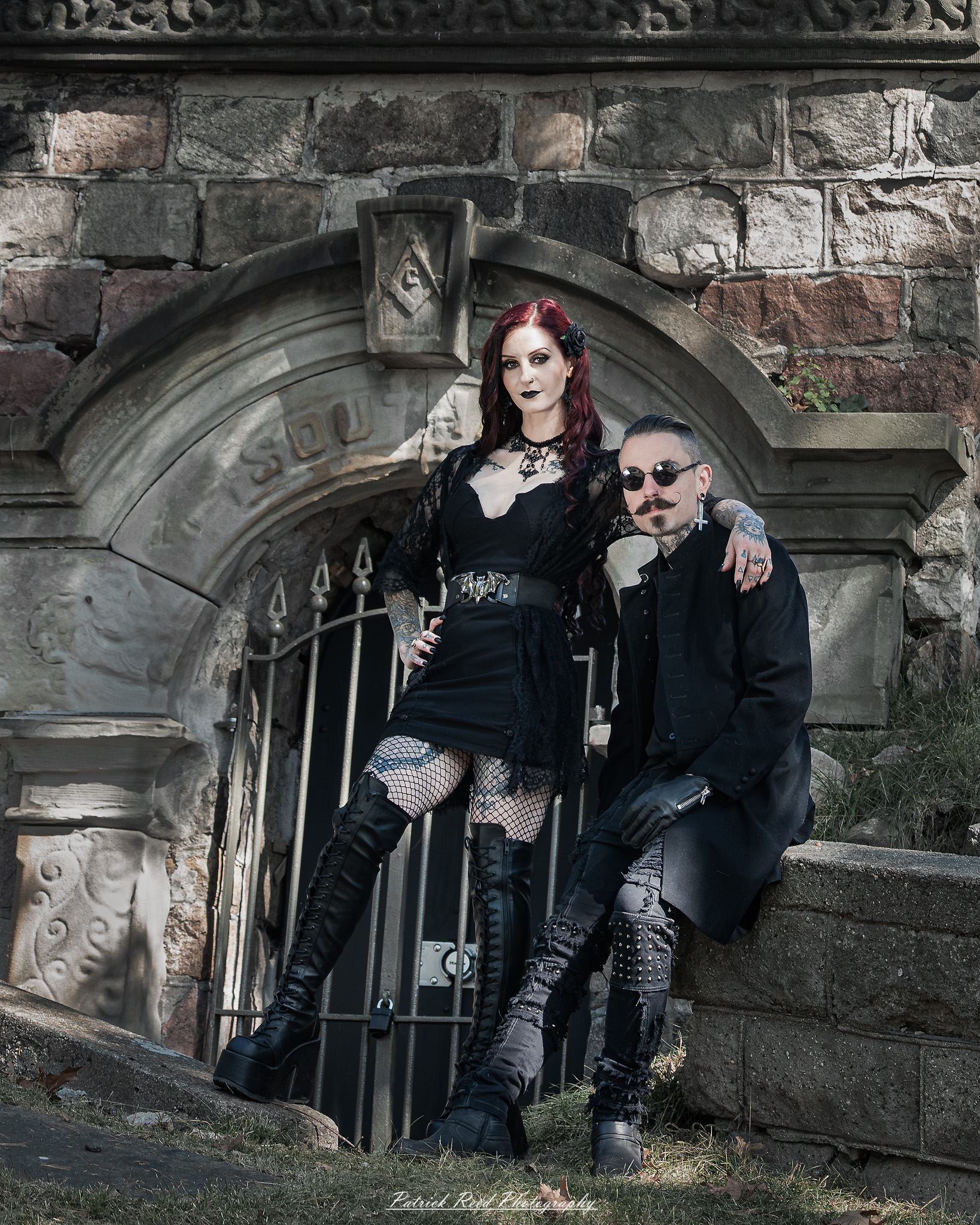 A gothic-themed portrait of a model named Minerva with a partner, photographed in a cemetery on September 28, 2025, featuring dark attire, moody lighting, and dramatic composition.