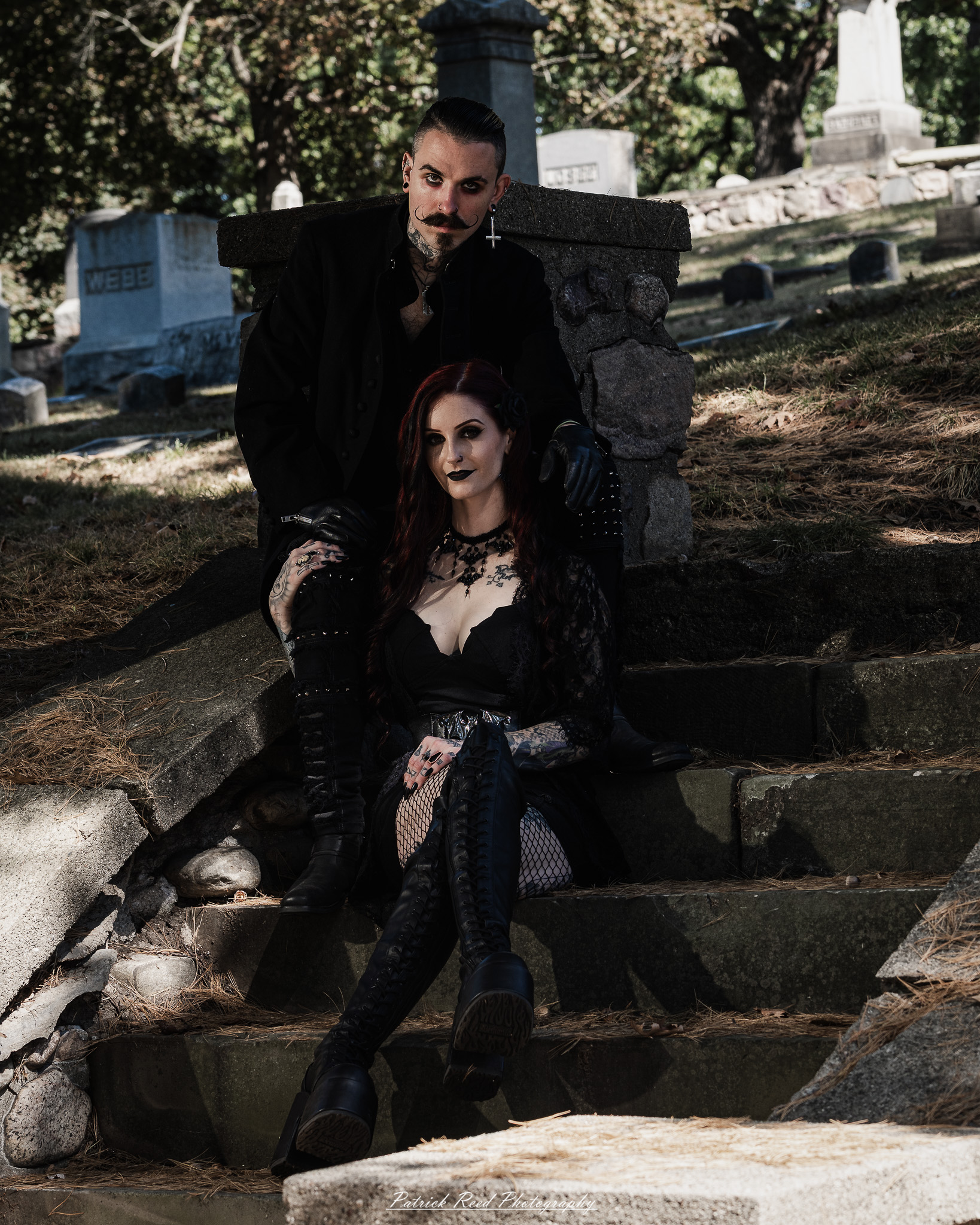 A gothic-themed portrait of a model named Minerva with a partner, photographed in a cemetery on September 28, 2025, featuring dark attire, moody lighting, and dramatic composition.