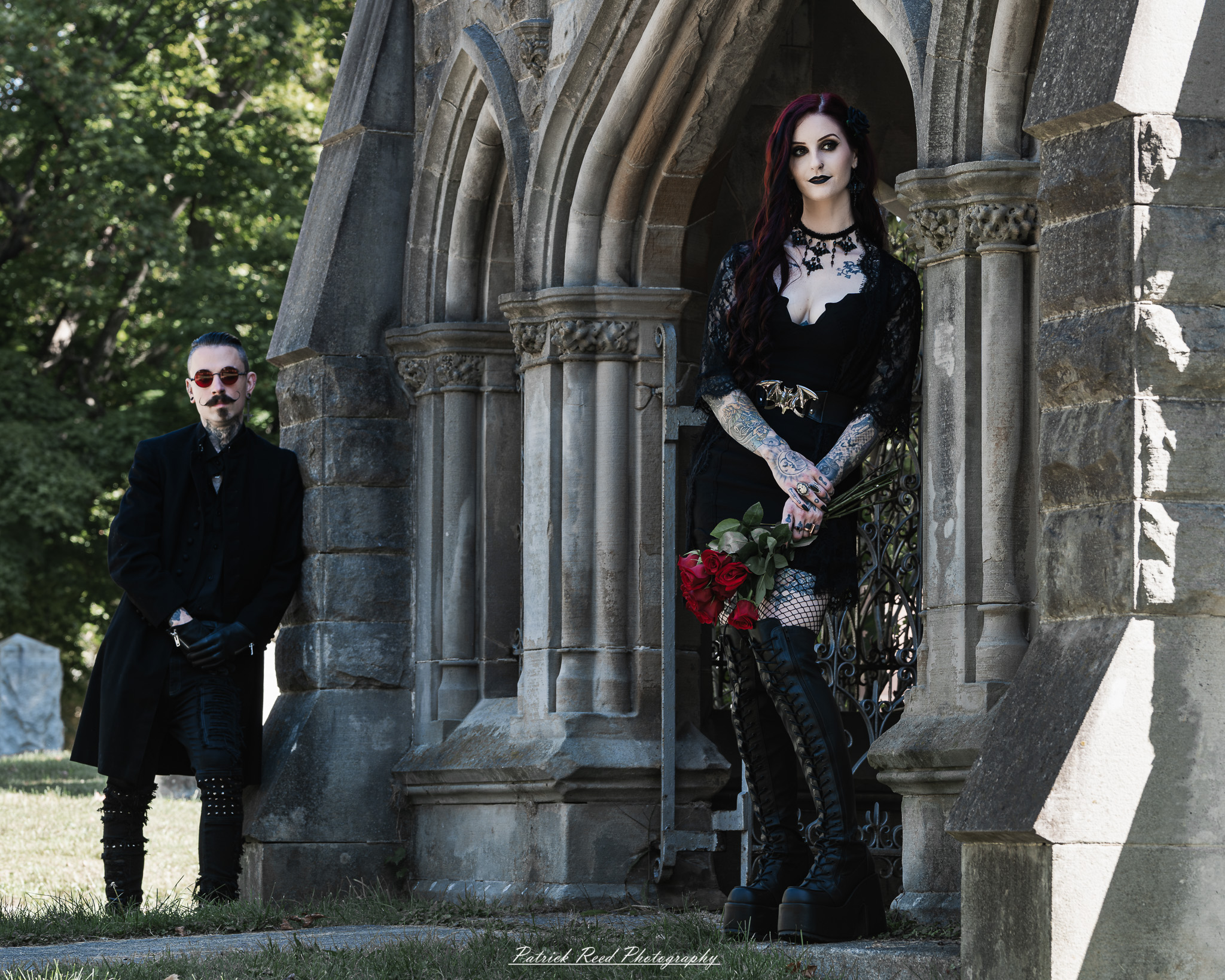 A gothic-themed portrait of a model named Minerva with a partner, photographed in a cemetery on September 28, 2025, featuring dark attire, moody lighting, and dramatic composition.