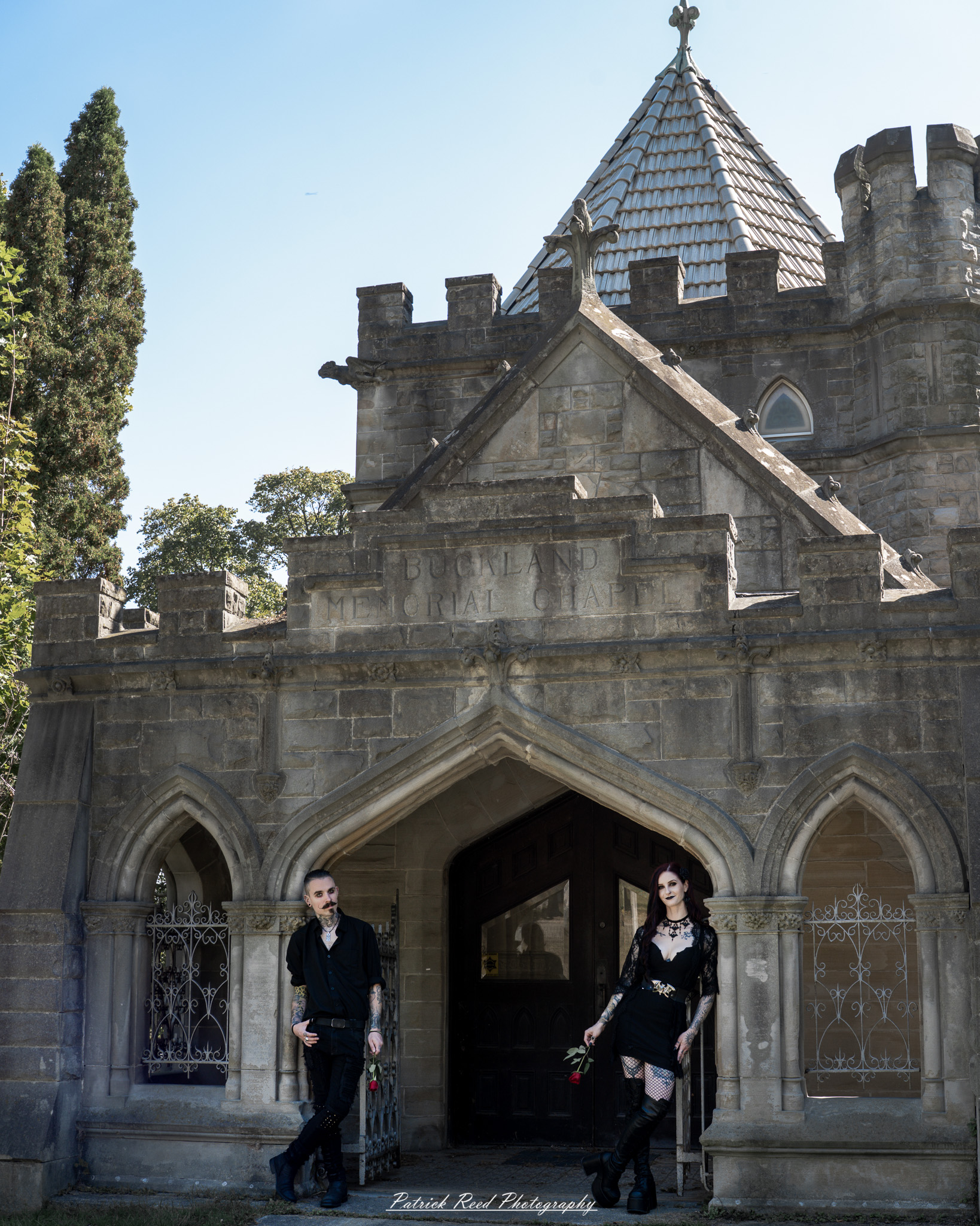 A gothic-themed portrait of a model named Minerva with a partner, photographed in a cemetery on September 28, 2025, featuring dark attire, moody lighting, and dramatic composition.