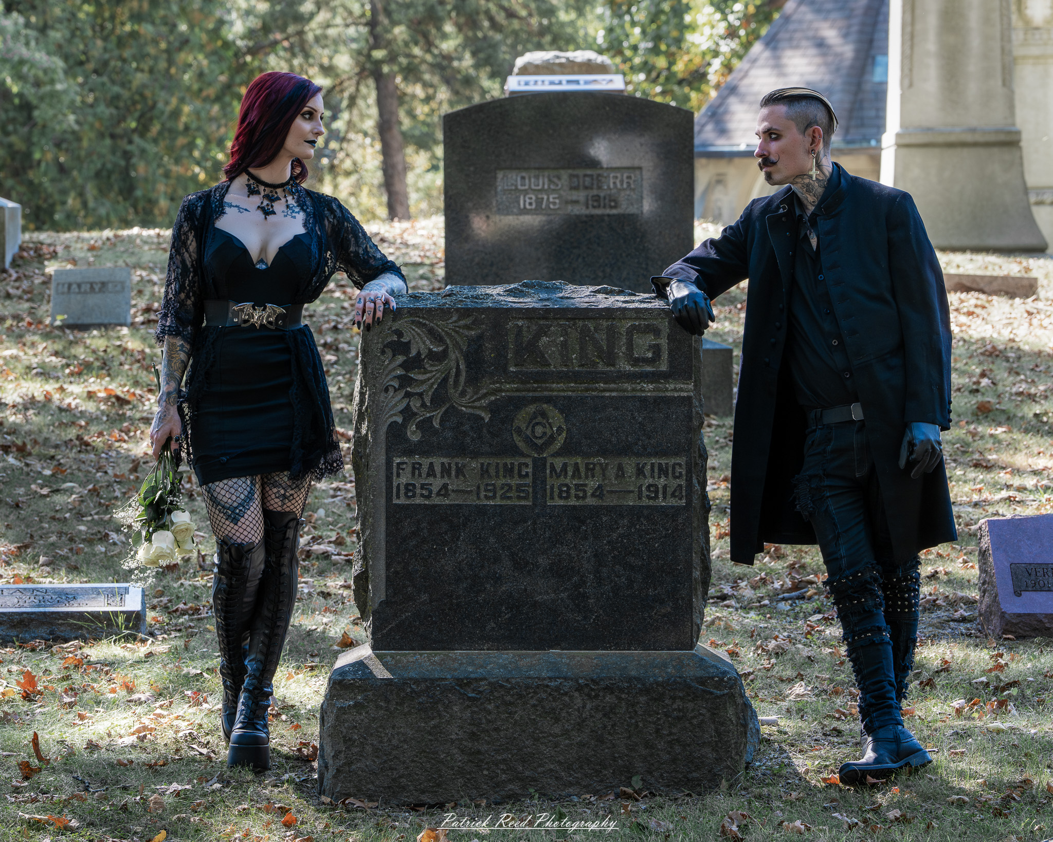 A gothic-themed portrait of a model named Minerva with a partner, photographed in a cemetery on September 28, 2025, featuring dark attire, moody lighting, and dramatic composition.