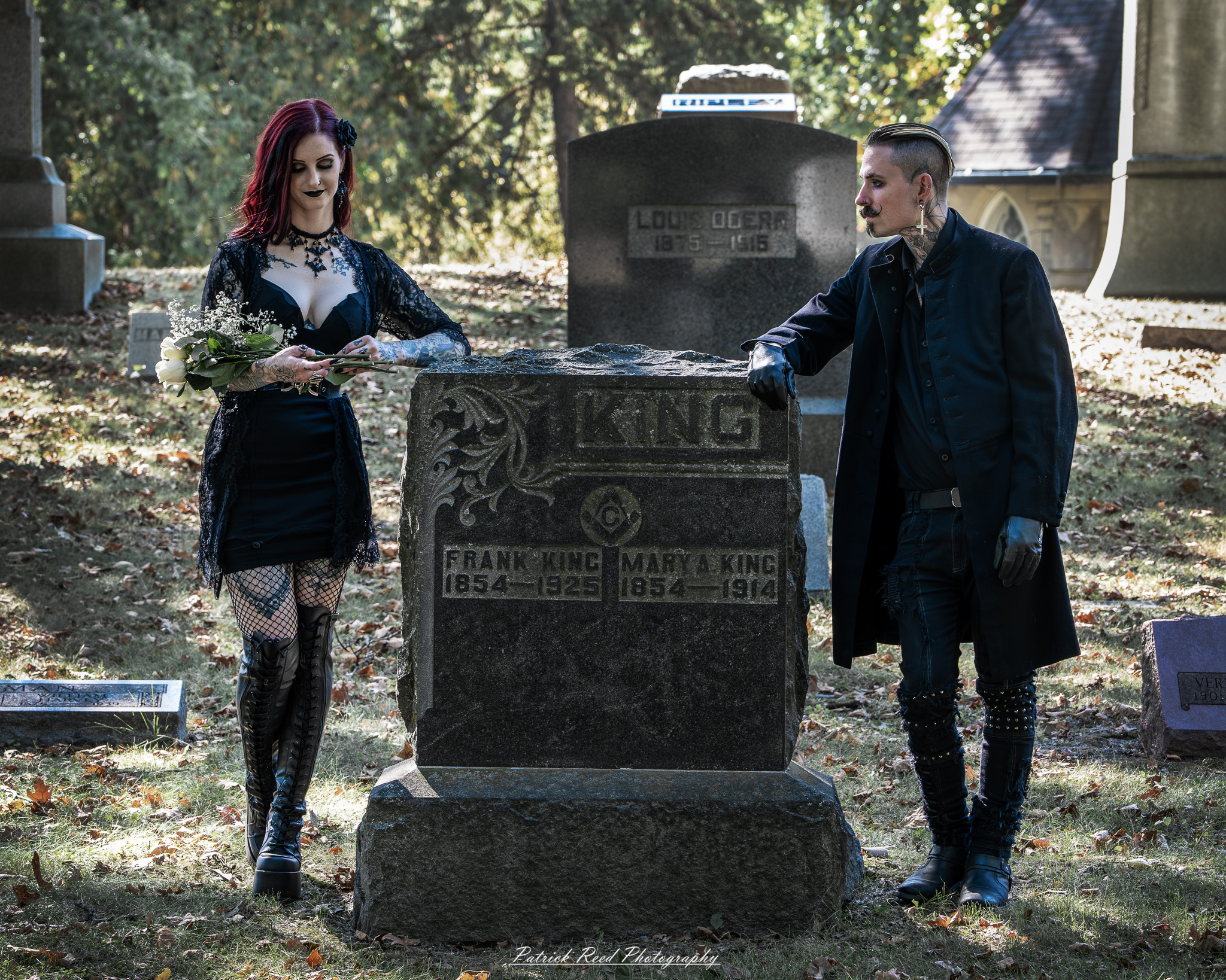 A gothic-themed portrait of a model named Minerva with a partner, photographed in a cemetery on September 28, 2025, featuring dark attire, moody lighting, and dramatic composition.