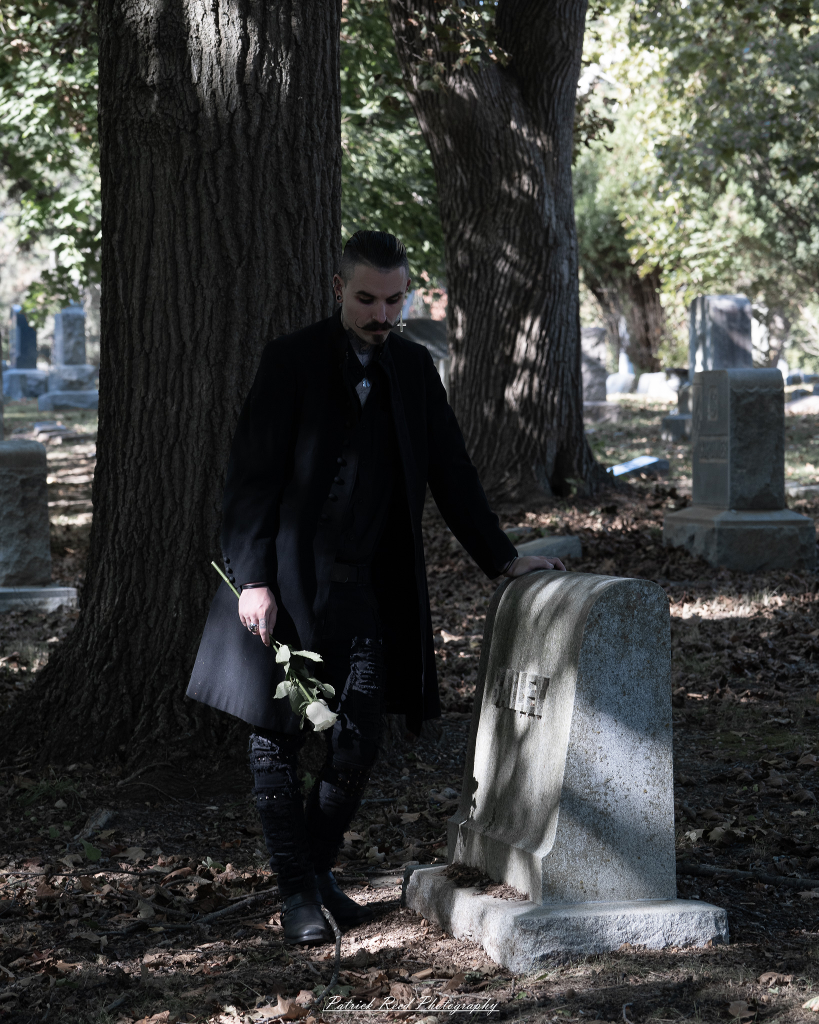 A gothic-themed portrait of a model named Minerva with a partner, photographed in a cemetery on September 28, 2025, featuring dark attire, moody lighting, and dramatic composition.