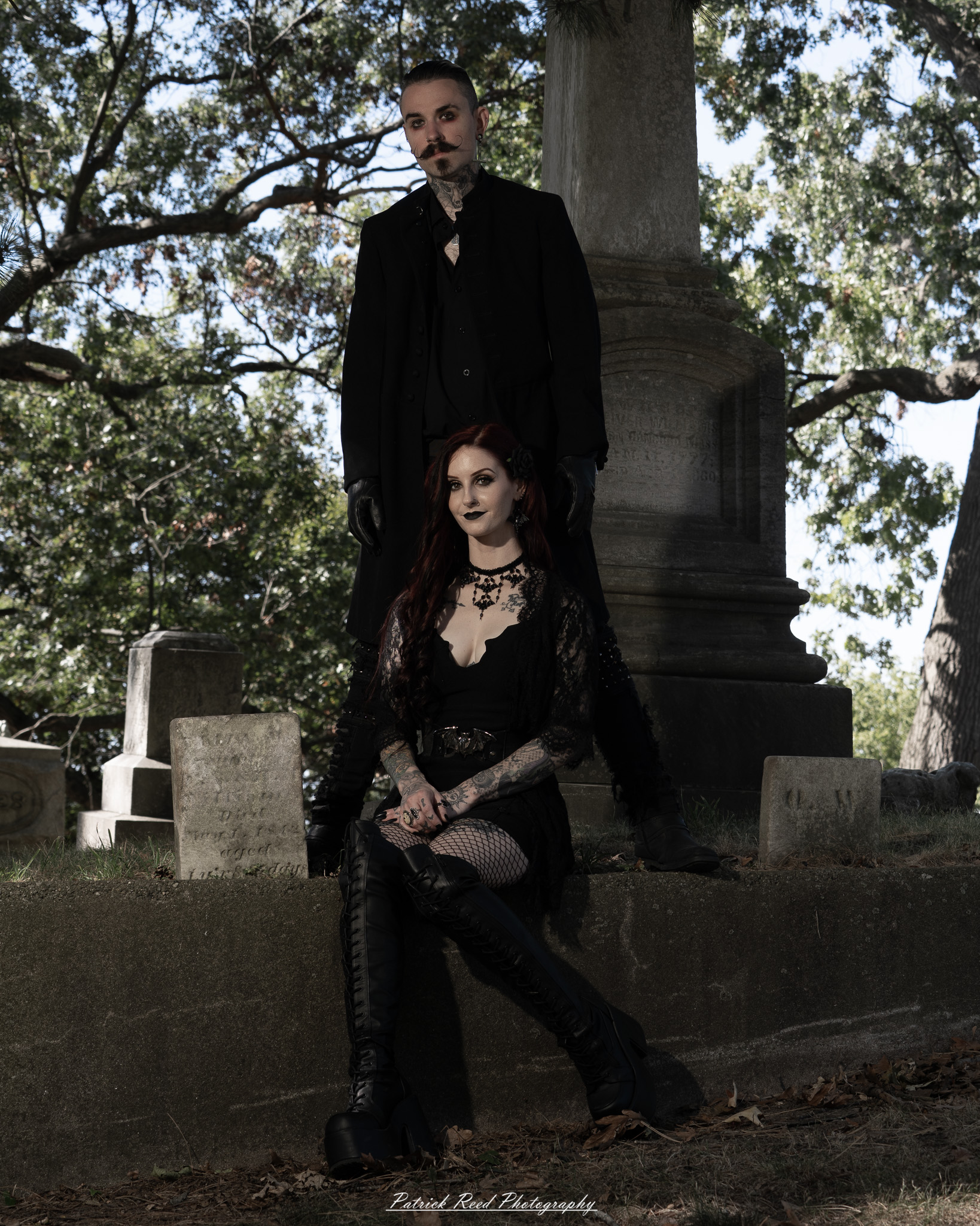 A gothic-themed portrait of a model named Minerva with a partner, photographed in a cemetery on September 28, 2025, featuring dark attire, moody lighting, and dramatic composition.