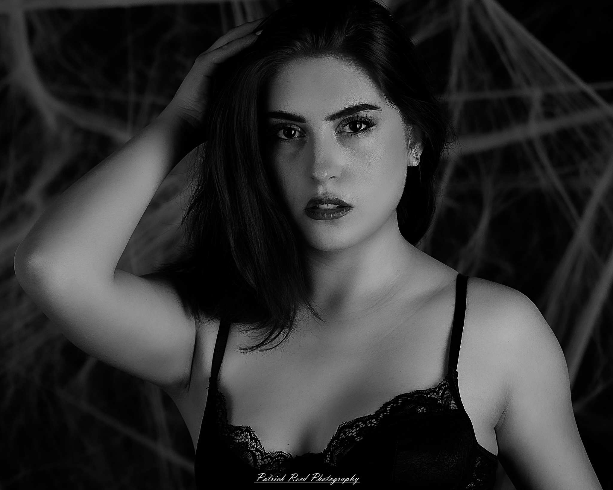 A portrait of a woman named Jinx surrounded by artificial spiderwebs, photographed on October 29, 2025. The lighting is dramatic and moody, emphasizing the texture of the webs and her expression.