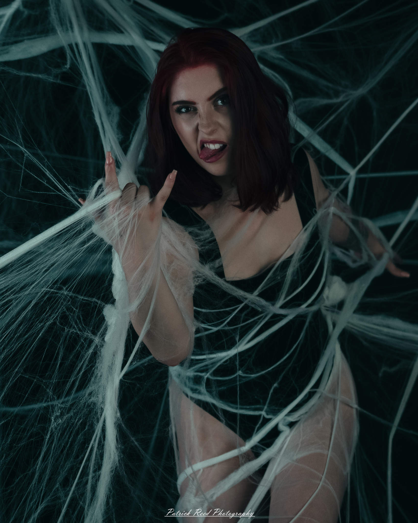 A portrait of a woman named Jinx surrounded by artificial spiderwebs, photographed on October 29, 2025. The lighting is dramatic and moody, emphasizing the texture of the webs and her expression.