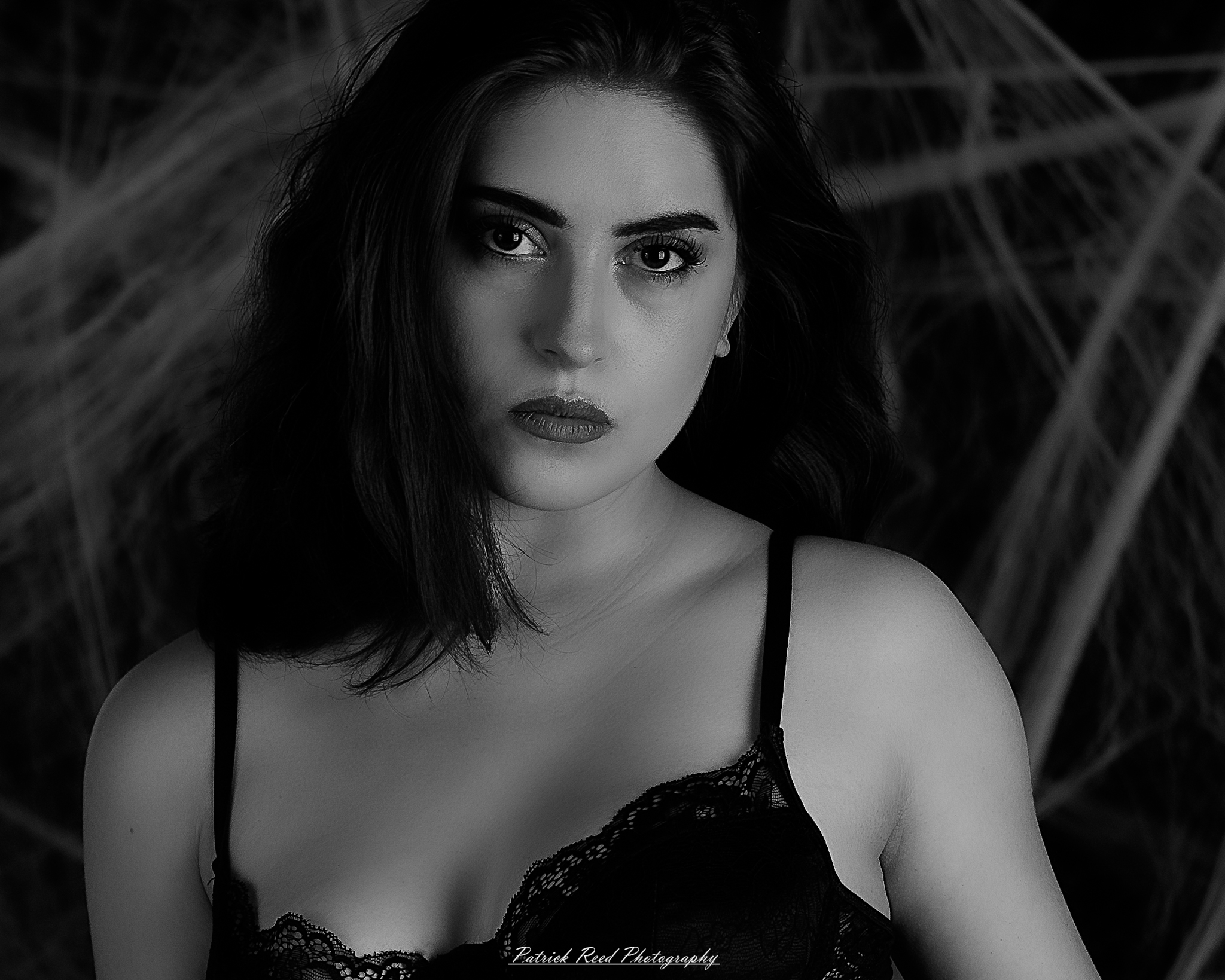 A portrait of a woman named Jinx surrounded by artificial spiderwebs, photographed on October 29, 2025. The lighting is dramatic and moody, emphasizing the texture of the webs and her expression.