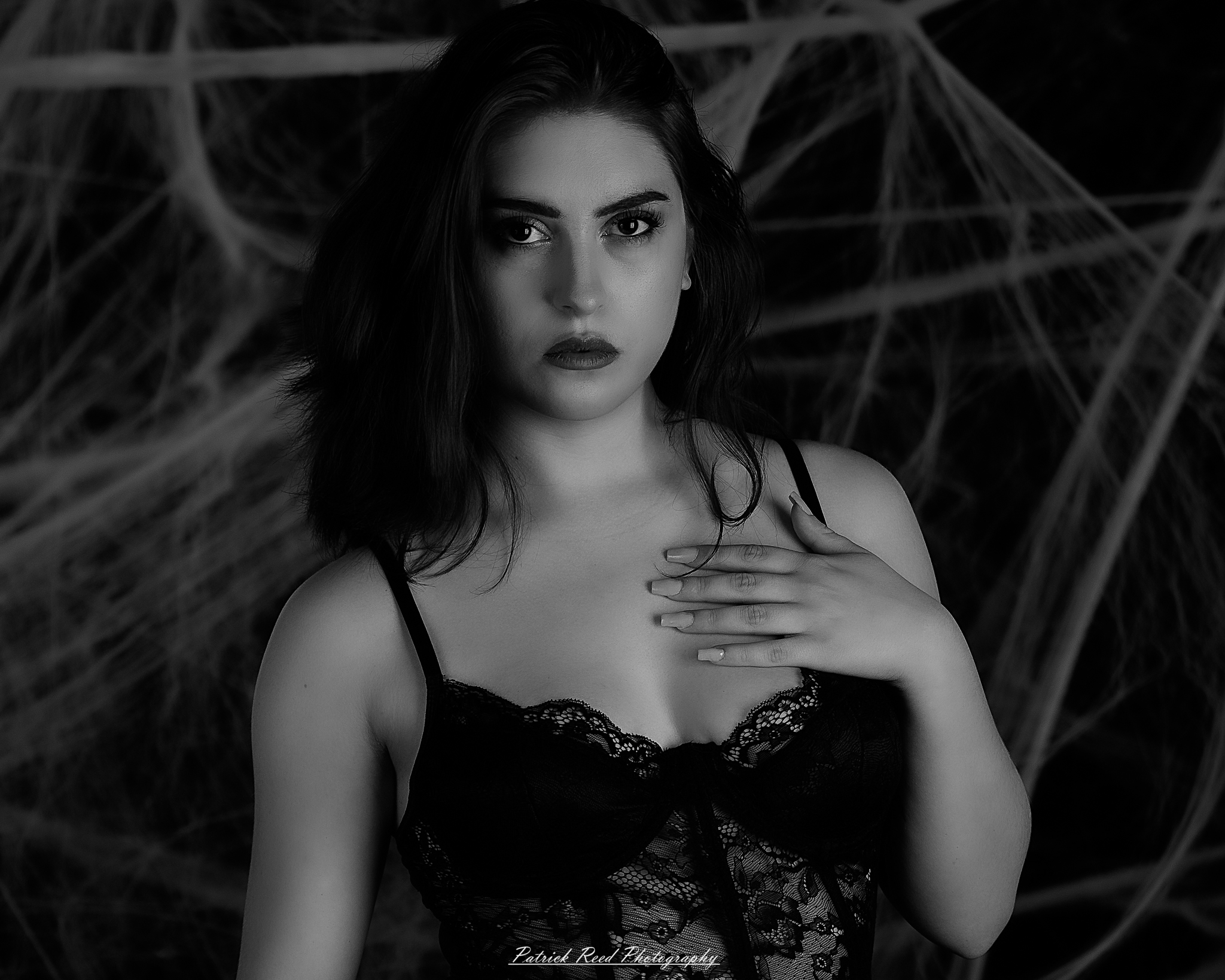 A portrait of a woman named Jinx surrounded by artificial spiderwebs, photographed on October 29, 2025. The lighting is dramatic and moody, emphasizing the texture of the webs and her expression.