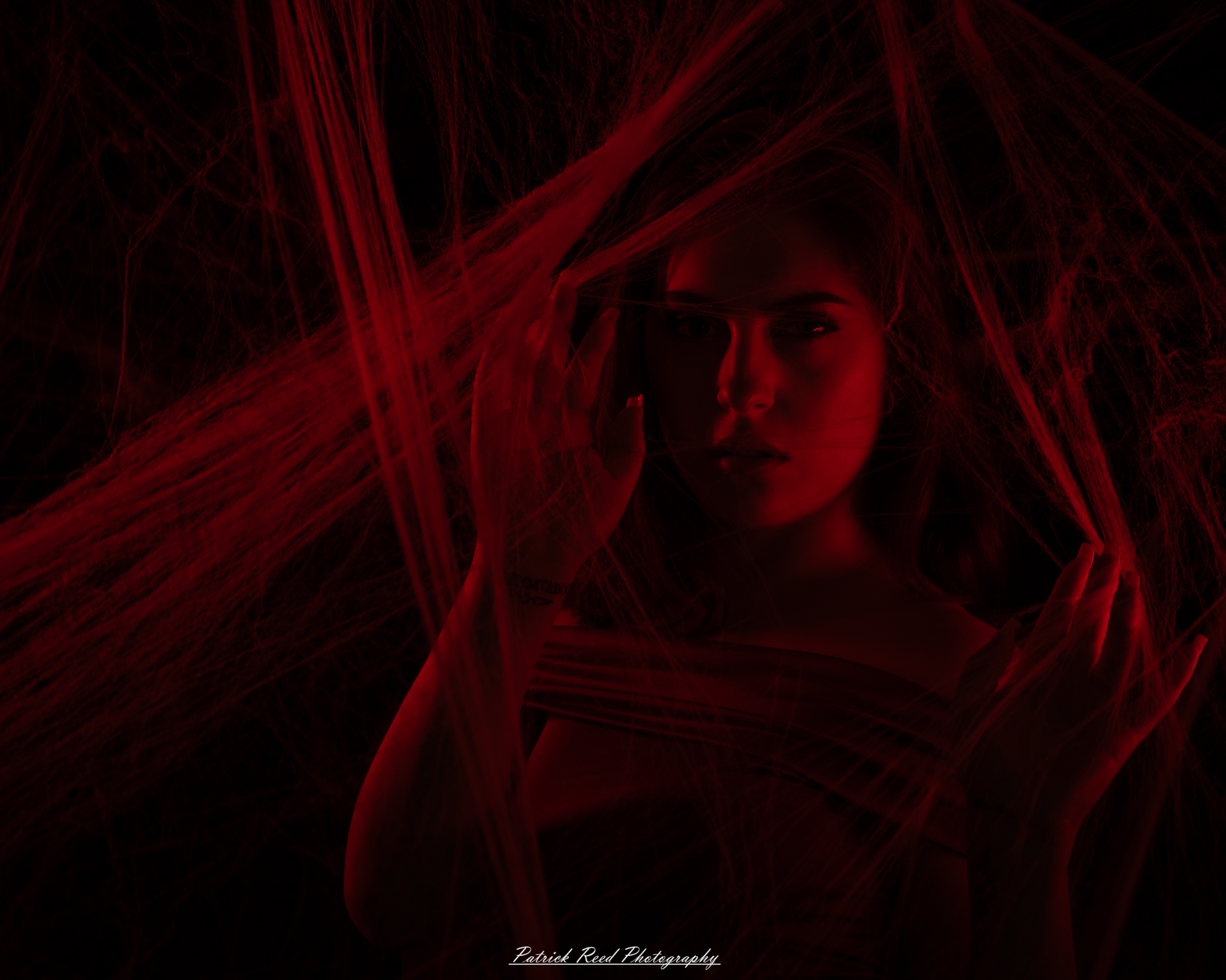 A portrait of a woman named Jinx surrounded by artificial spiderwebs, photographed on October 29, 2025. The lighting is dramatic and moody, emphasizing the texture of the webs and her expression.