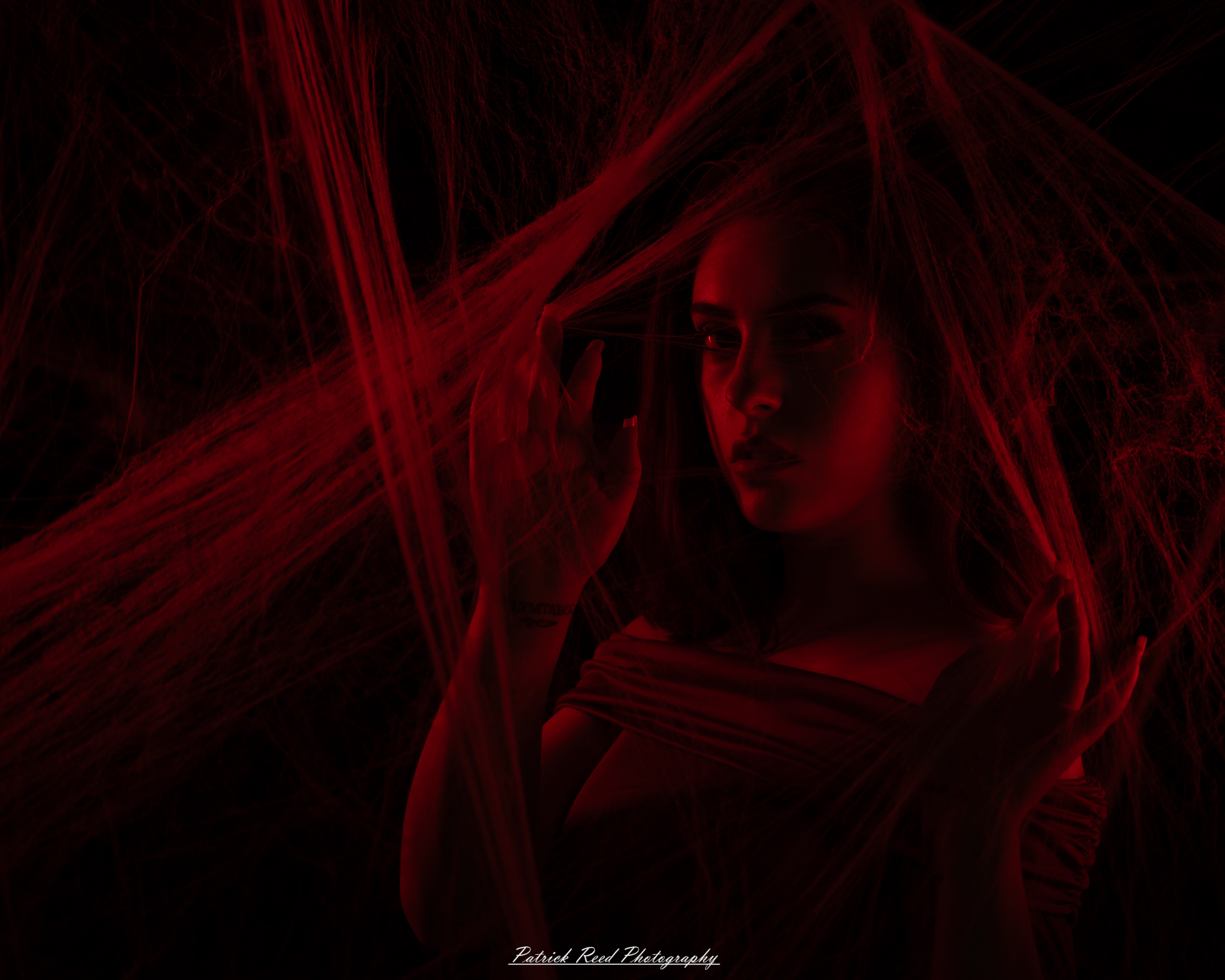 A portrait of a woman named Jinx surrounded by artificial spiderwebs, photographed on October 29, 2025. The lighting is dramatic and moody, emphasizing the texture of the webs and her expression.