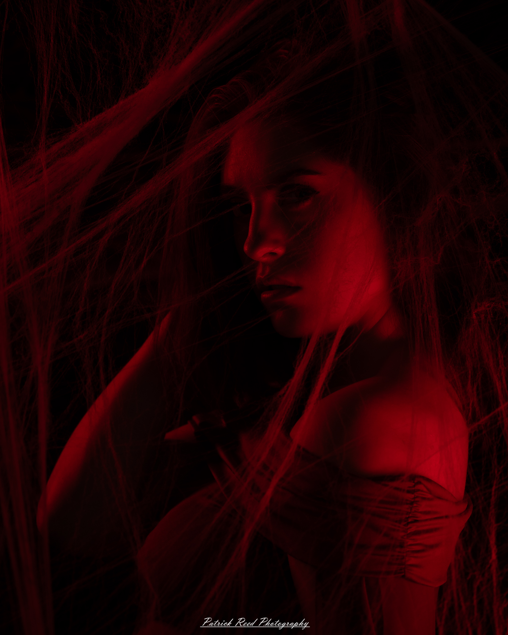 A portrait of a woman named Jinx surrounded by artificial spiderwebs, photographed on October 29, 2025. The lighting is dramatic and moody, emphasizing the texture of the webs and her expression.