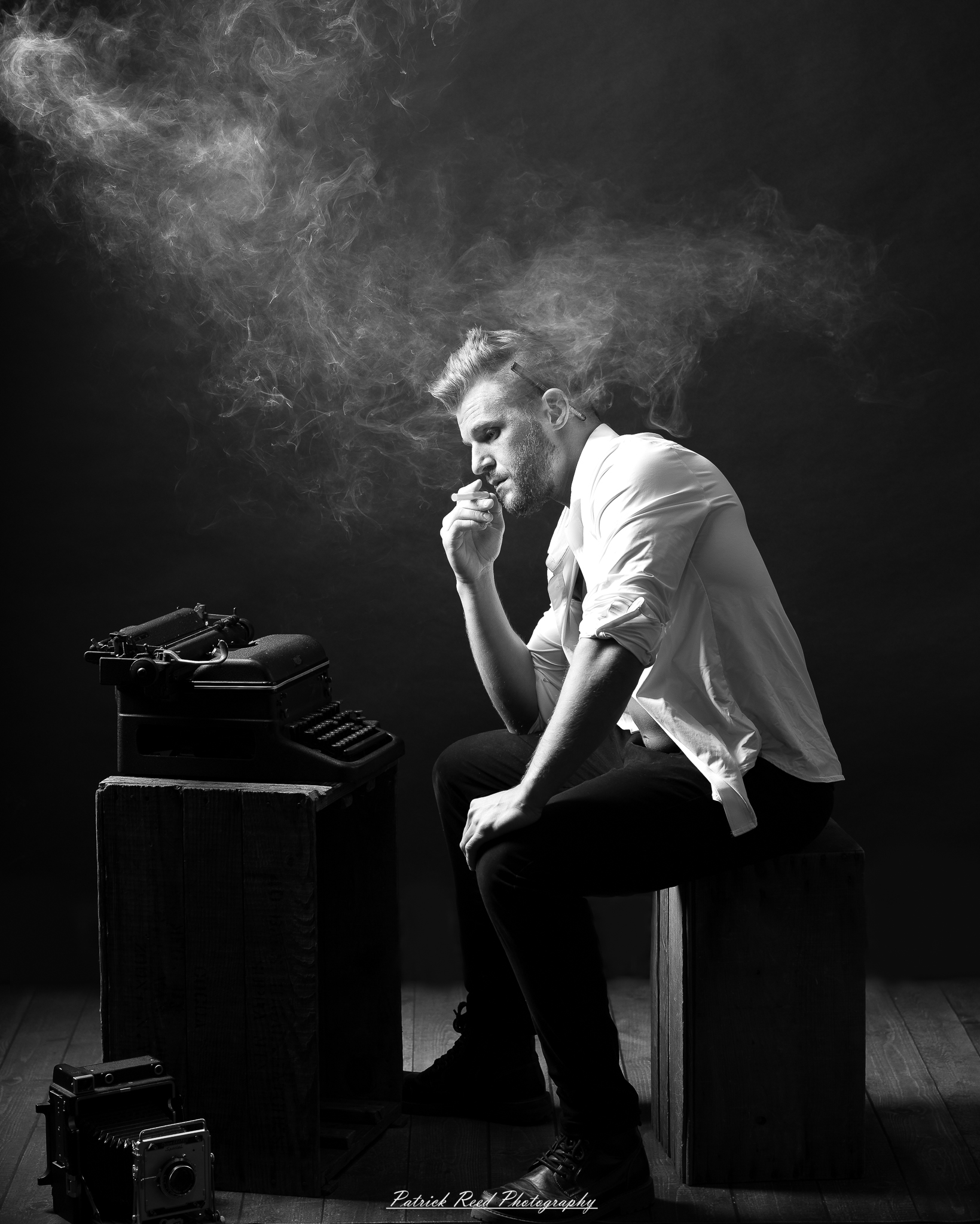 Black and white noir style portrait of a man sitting beside a vintage typewriter surrounded by drifting smoke
