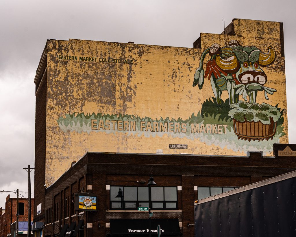 Large-scale mural in Eastern Market Detroit with layered graffiti textures and urban street art composition.