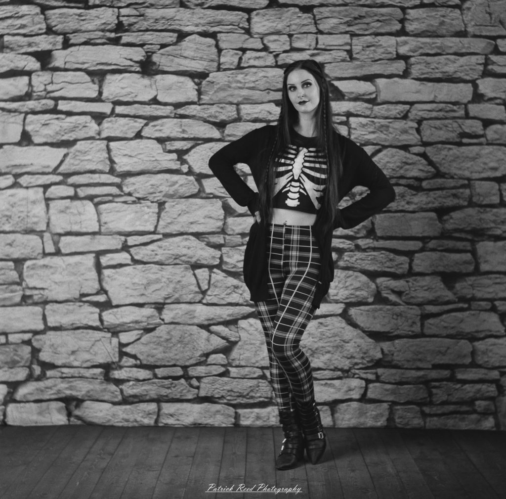 A medium format film portrait of a model styled in a casual goth look, photographed using a Mamiya C33 camera with moody studio lighting and classic analog texture.