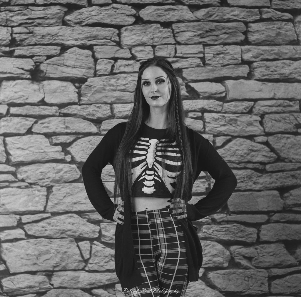 A medium format film portrait of a model styled in a casual goth look, photographed using a Mamiya C33 camera with moody studio lighting and classic analog texture.