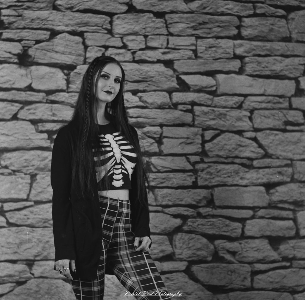 A medium format film portrait of a model styled in a casual goth look, photographed using a Mamiya C33 camera with moody studio lighting and classic analog texture.