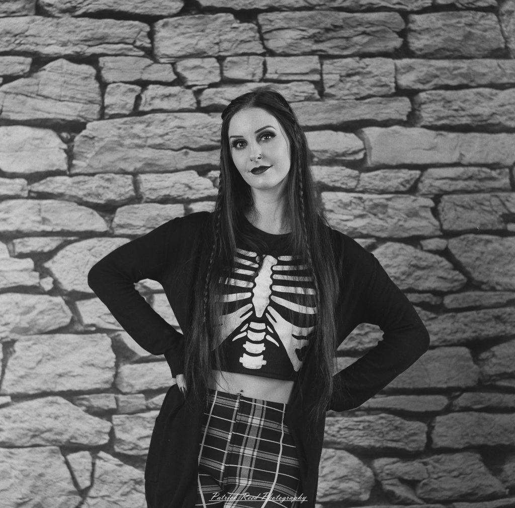 A medium format film portrait of a model styled in a casual goth look, photographed using a Mamiya C33 camera with moody studio lighting and classic analog texture.