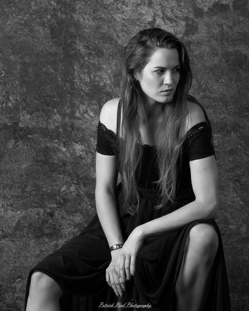 Close-up monochrome portrait of a woman seated, leaning forward with an intense expression.